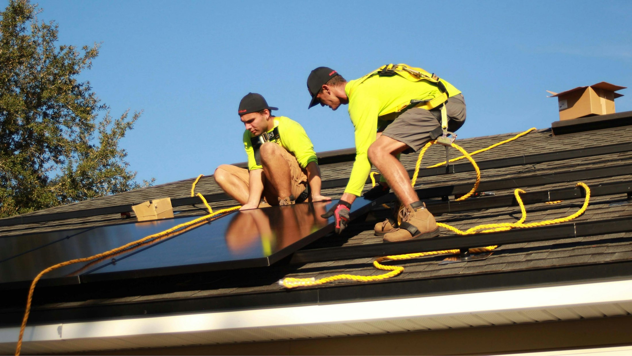 Zwei Monteure mit Absturzsicherung verlegen Solarmodule auf einem Dach