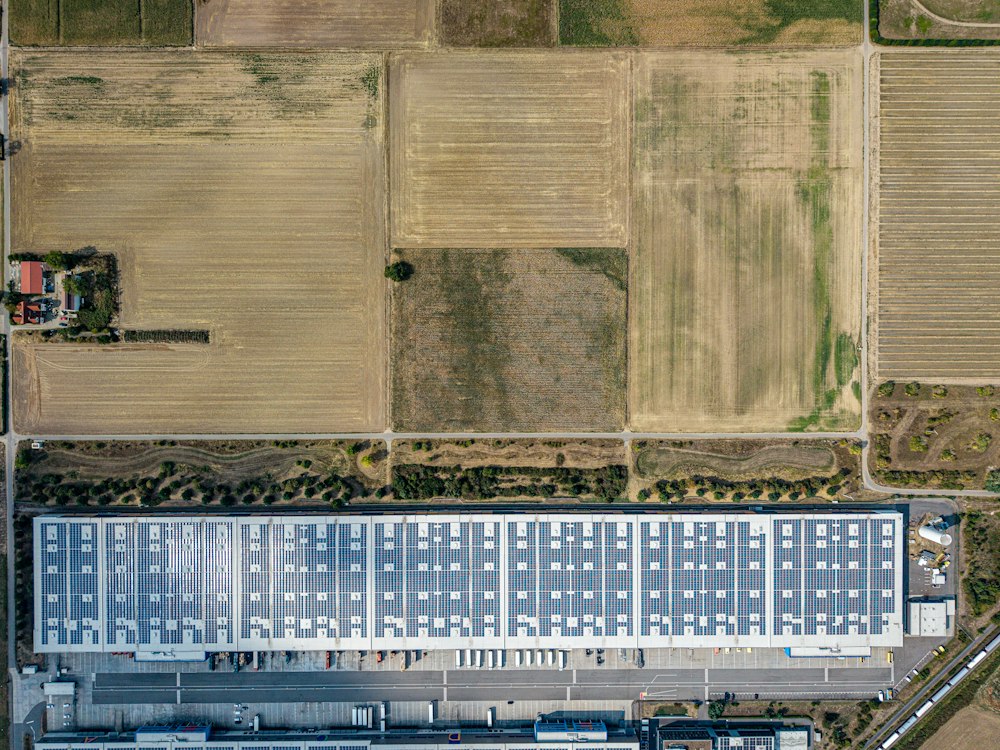 Luftbild einer Halle mit Solarmodulen zwischen Feldern
