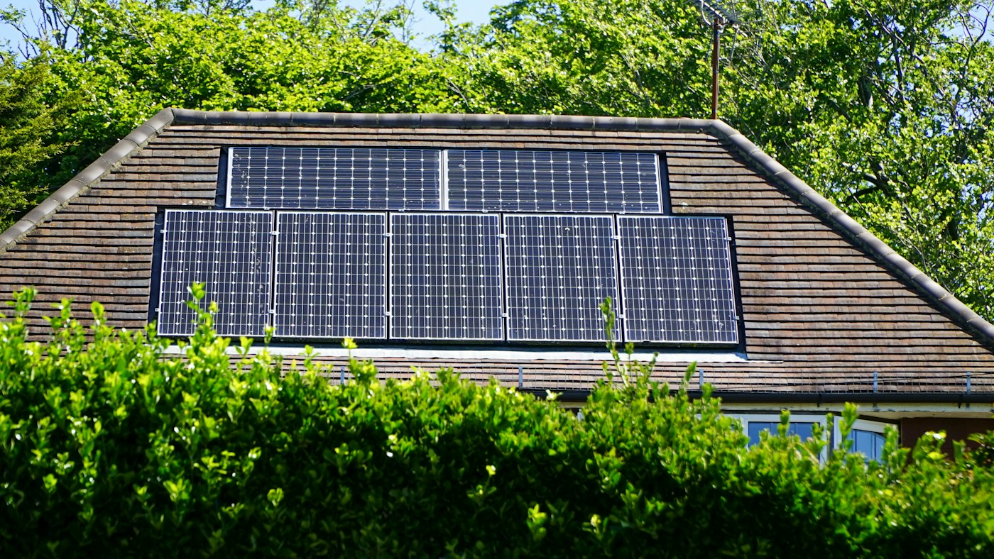 Wohnhaus mit Walmdach und Solarmodulen hinter einer Hecke