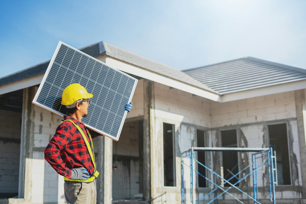 Monteur trägt ein Solarmodul vor einem Neubau