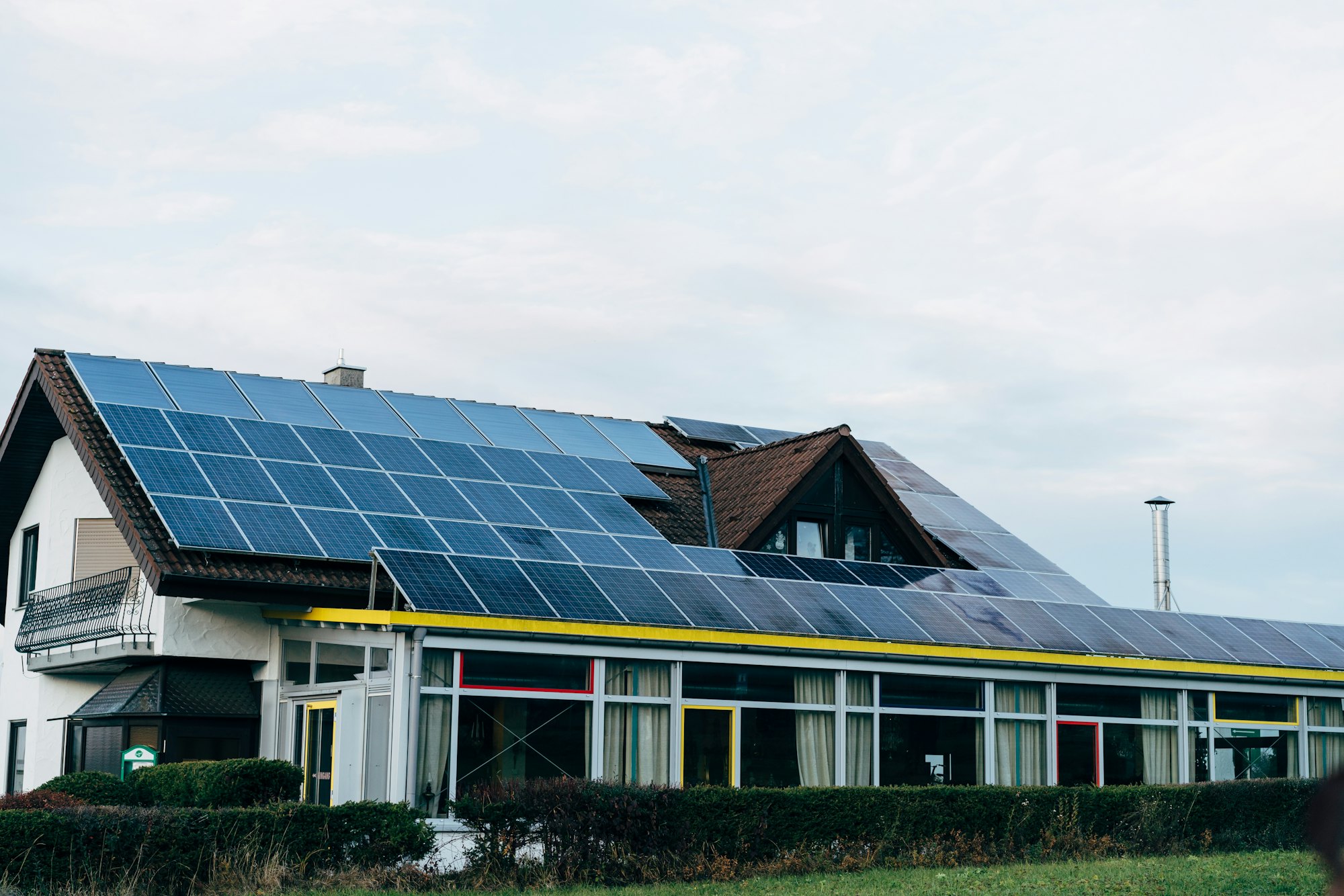 Wohnhaus mit großer Solaranlage auf dem Dach hinter einer Hecke